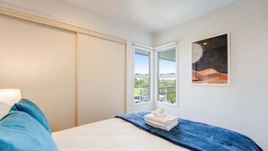 A bedroom with a bed, a window with a view, and a painting on the wall. - Henderson Retreat 3BR Townhouse with Parking (Auckland West)