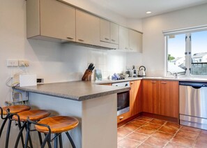 Una cocina con una isla central, taburetes de bar, armarios de madera y electrodomésticos de acero inoxidable, además de un ventanal con vistas.