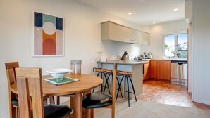 A modern kitchen with a dining area, featuring a round wooden table, bar stools, and a view to the outside. - Henderson Retreat 3BR Townhouse with Parking (Auckland West)