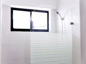 Un baño con azulejos blancos, un ventanal con detalles negros y una ducha con cabezal de ducha manual.