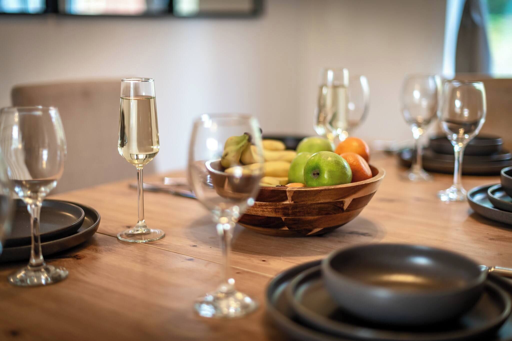 A wooden table with a fruit bowl, wine glasses, and a bowl.
