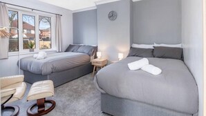 Un dormitorio con dos camas, una silla, una mesita de noche, un reloj y una ventana.