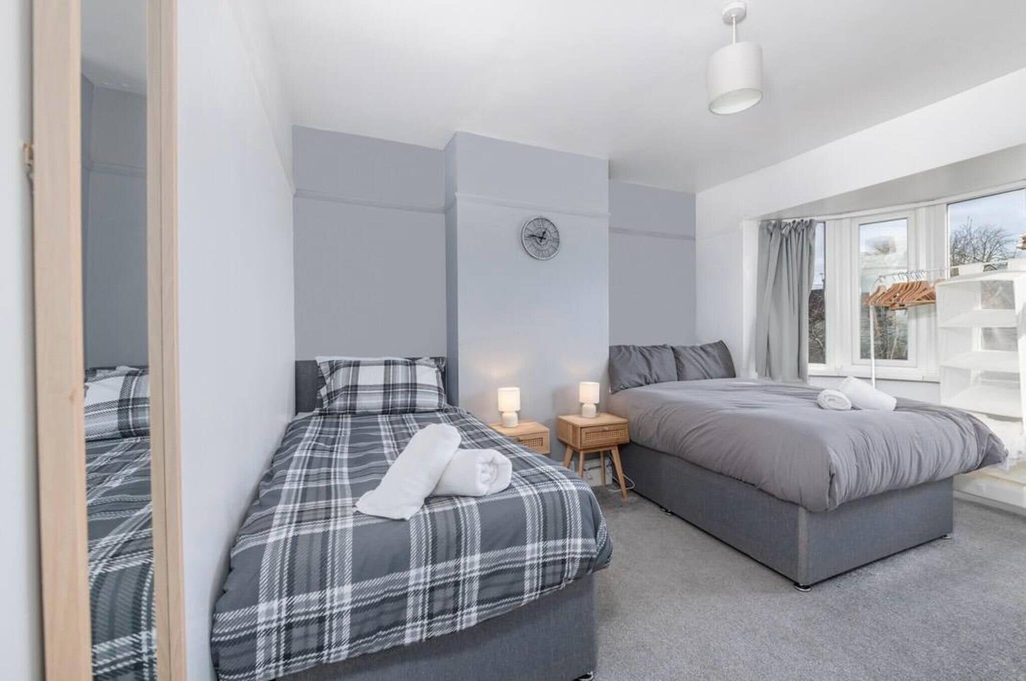 A hotel room with two beds, a clock on the wall, bedside lamps, and a view through the window.