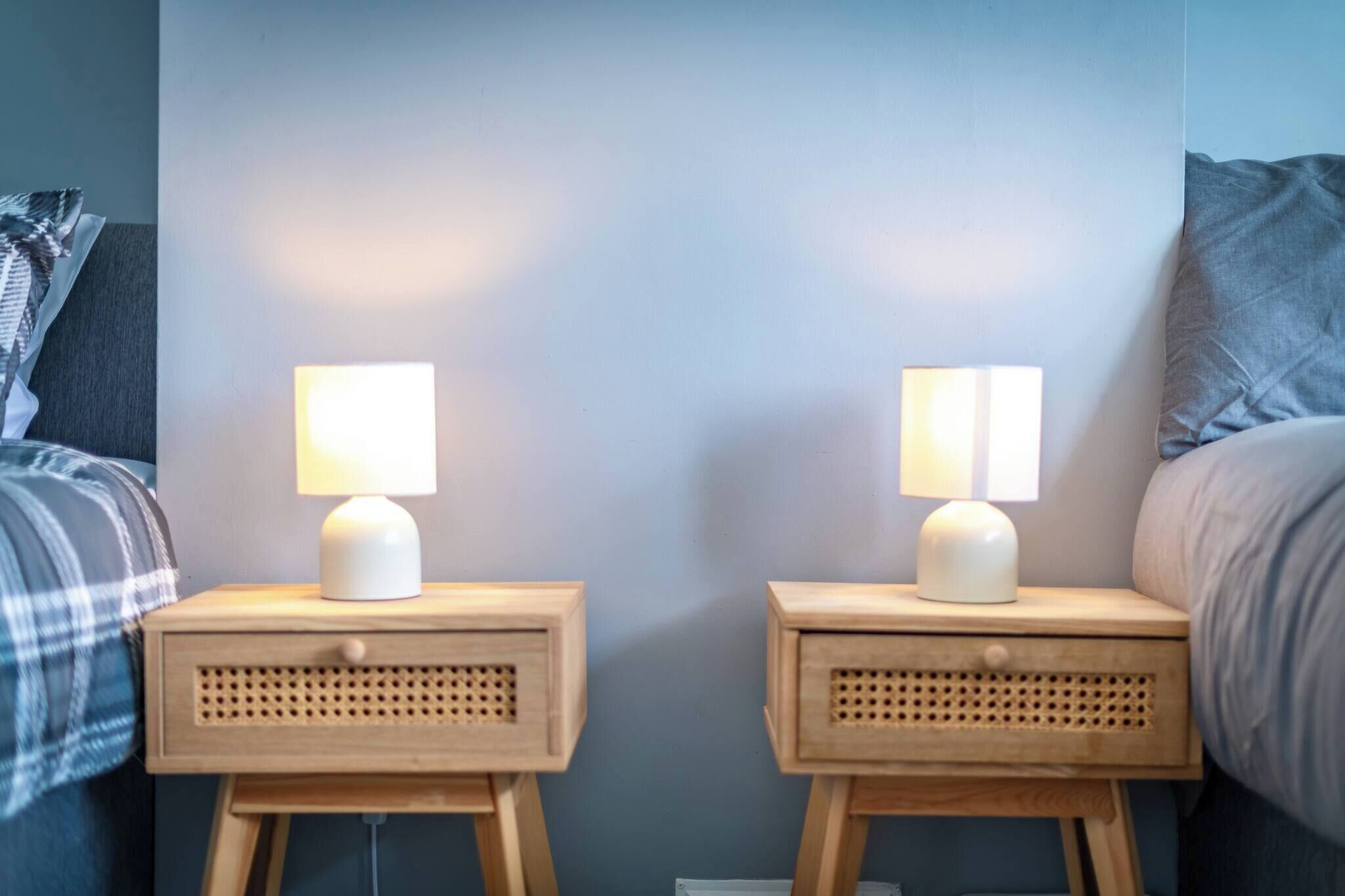 Two bedside tables with lamps, a bed with a grey blanket, and a wall with a blue accent.