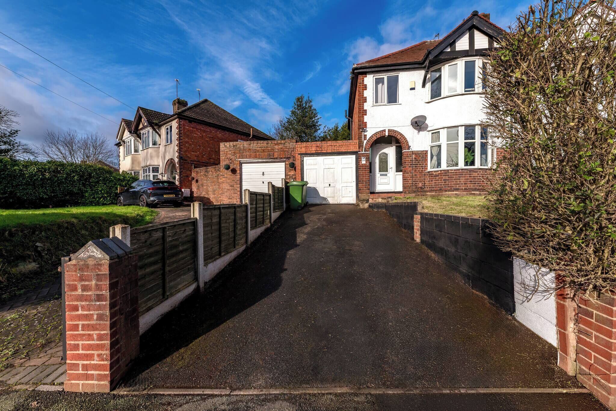 A residential street with houses, a driveway, and a brick wall.