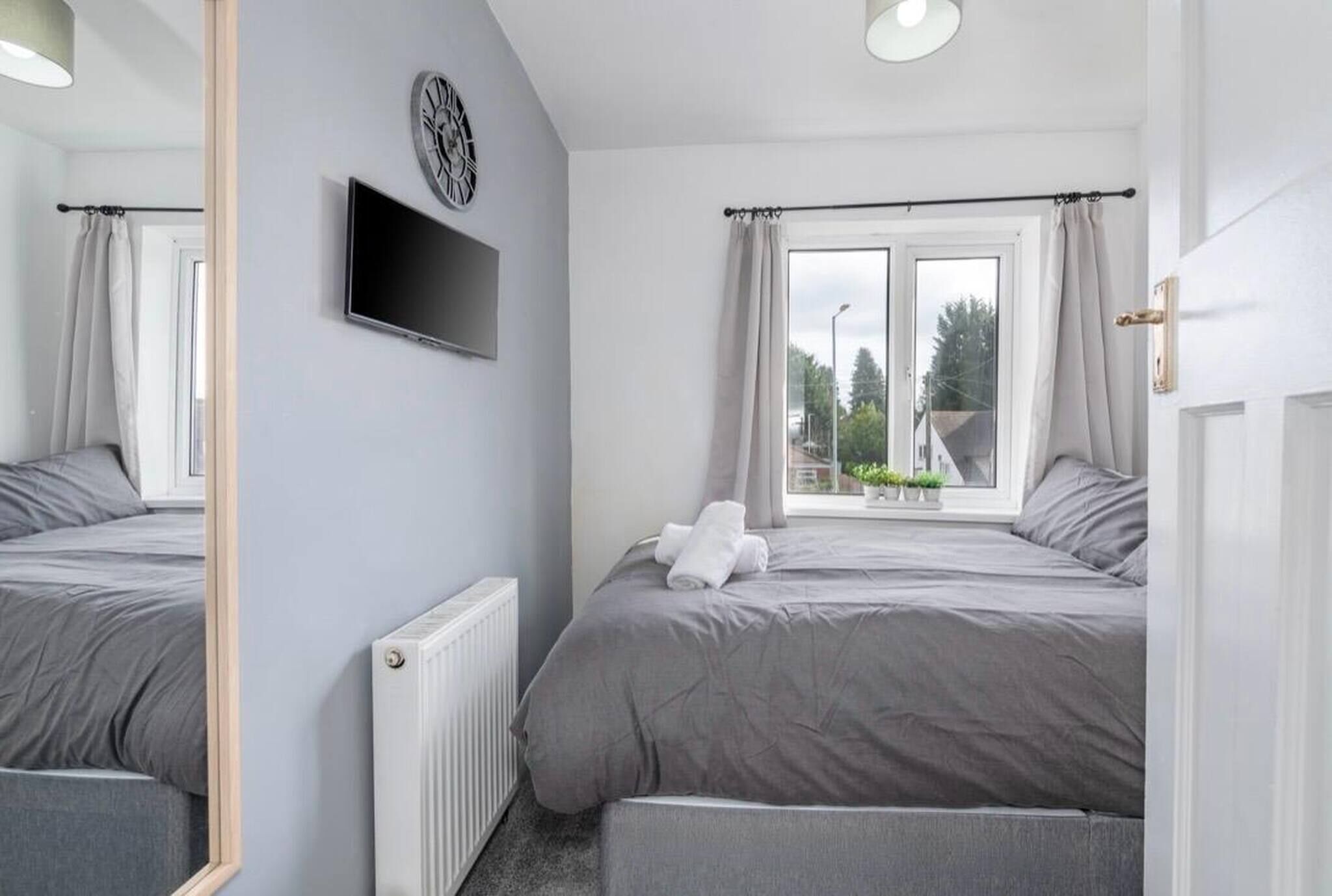 A bedroom with a bed, a TV, a window with curtains, and a radiator.