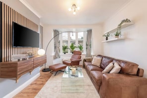 A living room with a flat-screen TV, leather sofa, and a glass coffee table. - Charming 3-bedroom Wolverhampton Home With Private Hot Tub (Wolverhampton)