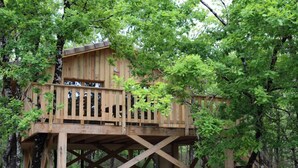 Una casa en el árbol de madera con balcón, construida sobre una estructura de madera robusta, rodeada de árboles.