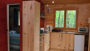 Una cabaña de madera acogedora con kitchenette, una cama con ropa de cama estampada y un ventanal con vista al bosque.