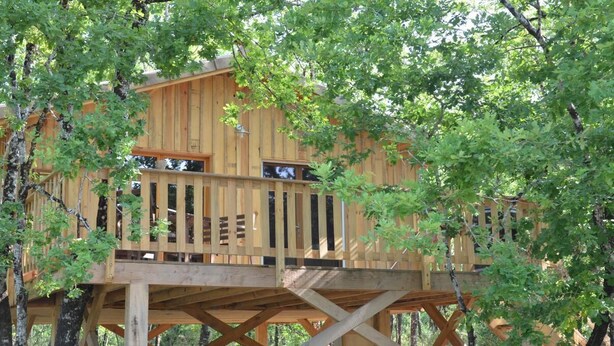 Una casa en el árbol de madera con balcón, construida sobre una sólida plataforma de madera.