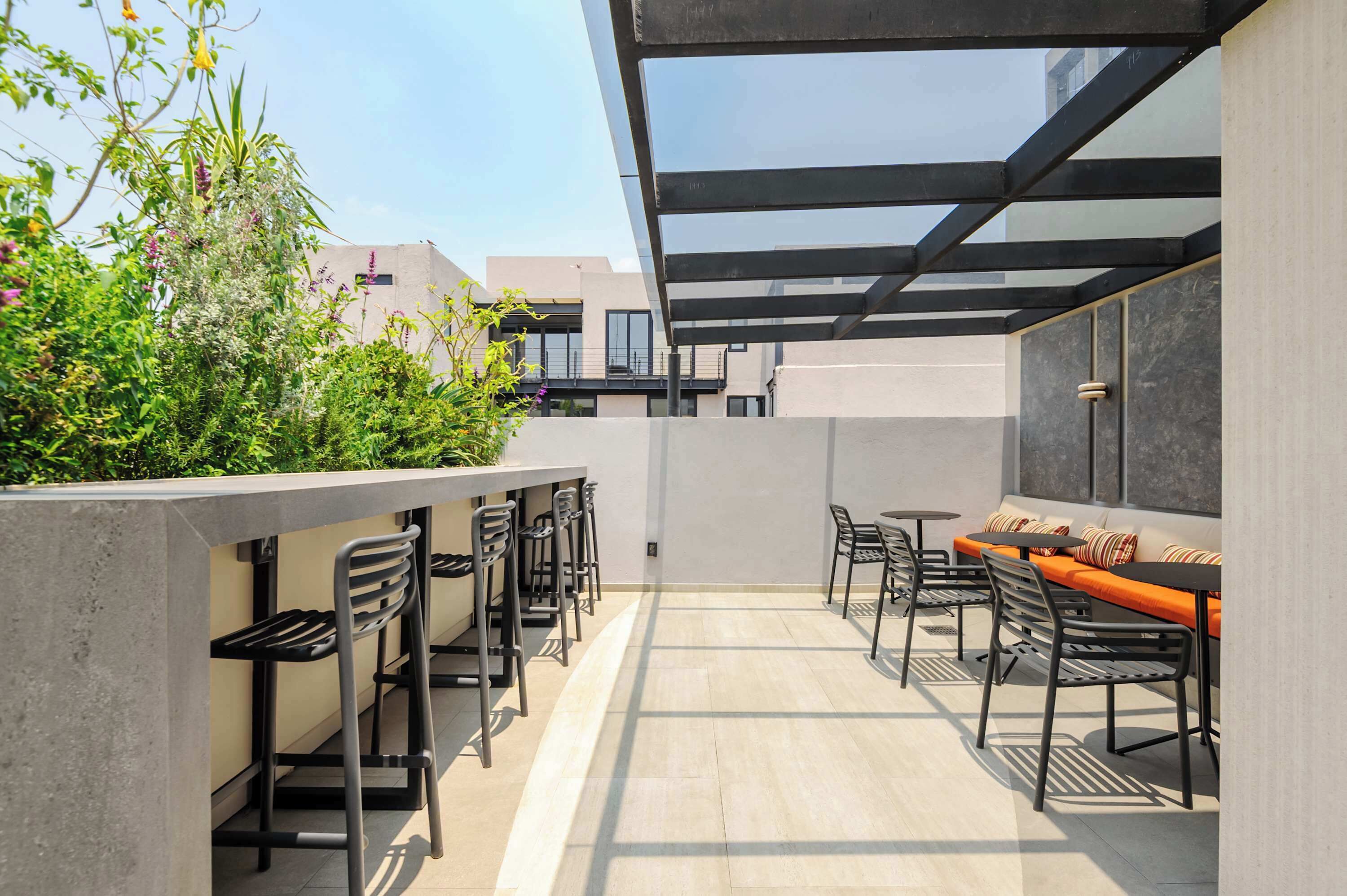 A rooftop terrace with outdoor seating, a glass ceiling, and a view of surrounding buildings.