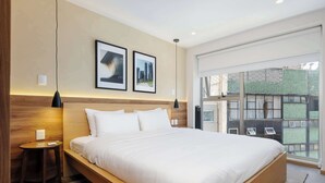 Une chambre d’hôtel moderne avec un grand lit, une petite table de chevet, une lampe fixée au mur et des tableaux encadrés.