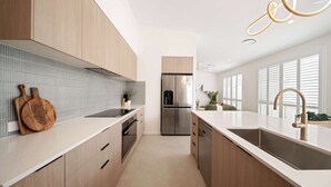 A modern kitchen with wooden cabinets, a stainless steel refrigerator, and a large island with a sink. - Sage Palmview - Home Away From Home (Mooloolaba Region)