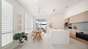 A modern kitchen with a central island, wooden cabinets, and a dining area with a table and chairs. - Sage Palmview - Home Away From Home (Mooloolaba Region)