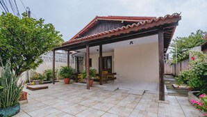 Un patio couvert doté d’un sol carrelé, de plantes en pot et d’une structure en bois formant une pergola.