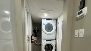 A laundry room with two stacked washers and dryers, a fire extinguisher, and a thermostat on the wall. - The Urban Retreat (Calgary)