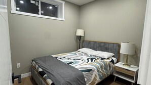 A bedroom with a bed, two bedside tables with lamps, a window, and a ceiling light. - The Urban Retreat (Calgary)