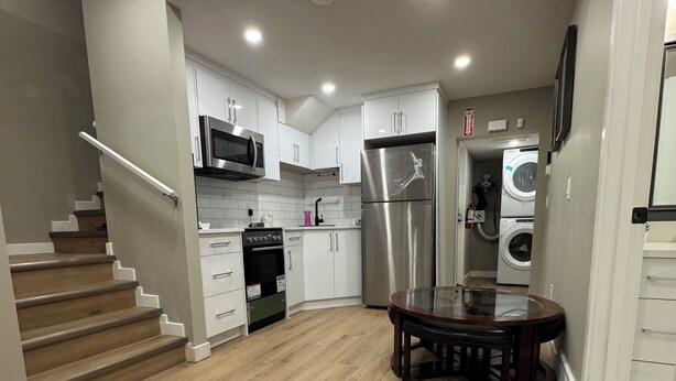 A modern kitchen with white cabinets, stainless steel appliances, and a wooden floor. - The Urban Retreat (Calgary)