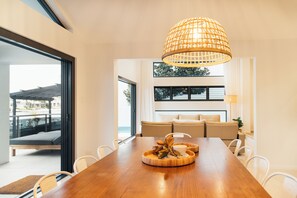 Ein zeitgemäßer Essbereich mit Holztisch, weißen Stühlen, einer gewobenen Pendelleuchte und Blick ins Freie.