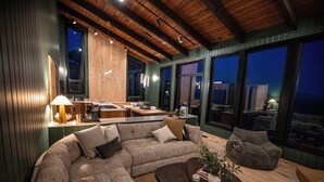 A modern living room with a sectional sofa, a coffee table, and a bean bag chair. There is a kitchen area in the background with a dining table and chairs. - Sunshine Ridge View - New Remodel - New Listing! (Anchorage)