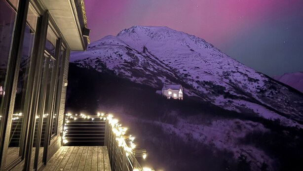 A snow-covered mountain with a house at the base, under a night sky with aurora borealis. - Sunshine Ridge View - New Remodel - New Listing! (Anchorage)