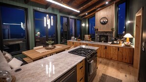 A modern kitchen with a large island, wooden cabinets, and a stone fireplace. - Sunshine Ridge View - New Remodel - New Listing! (Anchorage)