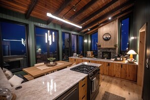A modern kitchen with a large island, wooden cabinets, and a stone fireplace. - Sunshine Ridge View - New Remodel - New Listing! (Anchorage)