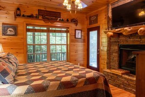 Un dormitorio de cabaña rústica con una cama grande, una chimenea, un televisor y una ventana con vistas al bosque.