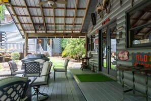 Un espace extérieur aménagé avec des sièges et une table, protégé par un auvent, une terrasse avec un tapis vert, et un bâtiment orné d’une enseigne Coca-Cola et d’une vieille enseigne « Old Times ».