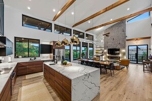 A modern kitchen with a large island, wooden beams, and large windows. - Lake Travis Private Dock + Boat Slip + Hot Tub (Briarcliff)