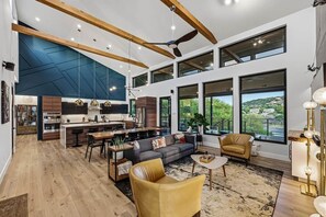 A spacious living area with a kitchen, dining table, sofa, and large windows offering a view. - Lake Travis Private Dock + Boat Slip + Hot Tub (Briarcliff)