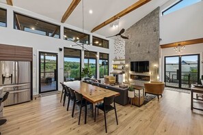 A spacious kitchen with a dining area, a fireplace, and large windows offering a view of the outdoors. - Lake Travis Private Dock + Boat Slip + Hot Tub (Briarcliff)