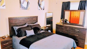Een slaapkamer met een bed, dressoir, nachtkastje en een spiegel.