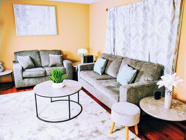Ein Wohnzimmer mit zwei grauen Sofas, einem runden Couchtisch, einem kleinen Beistelltisch und einem Blumentopf.