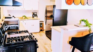 Een moderne keuken met een gasfornuis, roestvrijstalen apparatuur, witte kasten en een bar met een zwarte stoel.