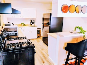 Una cocina moderna con estufa a gas, electrodomésticos de acero inoxidable, armarios blancos y una zona de bar con una silla negra.