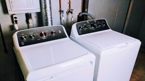 Twee witte wasmachines met voorlader en bedieningspanelen, aangesloten op een boiler en leidingen.