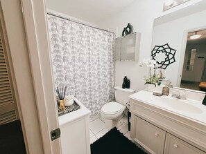 A bathroom with a toilet, a sink, a mirror, and a shower curtain with a pattern. - EaDo Treasure with Private Garage Near Downtown and Stadiums (Houston)
