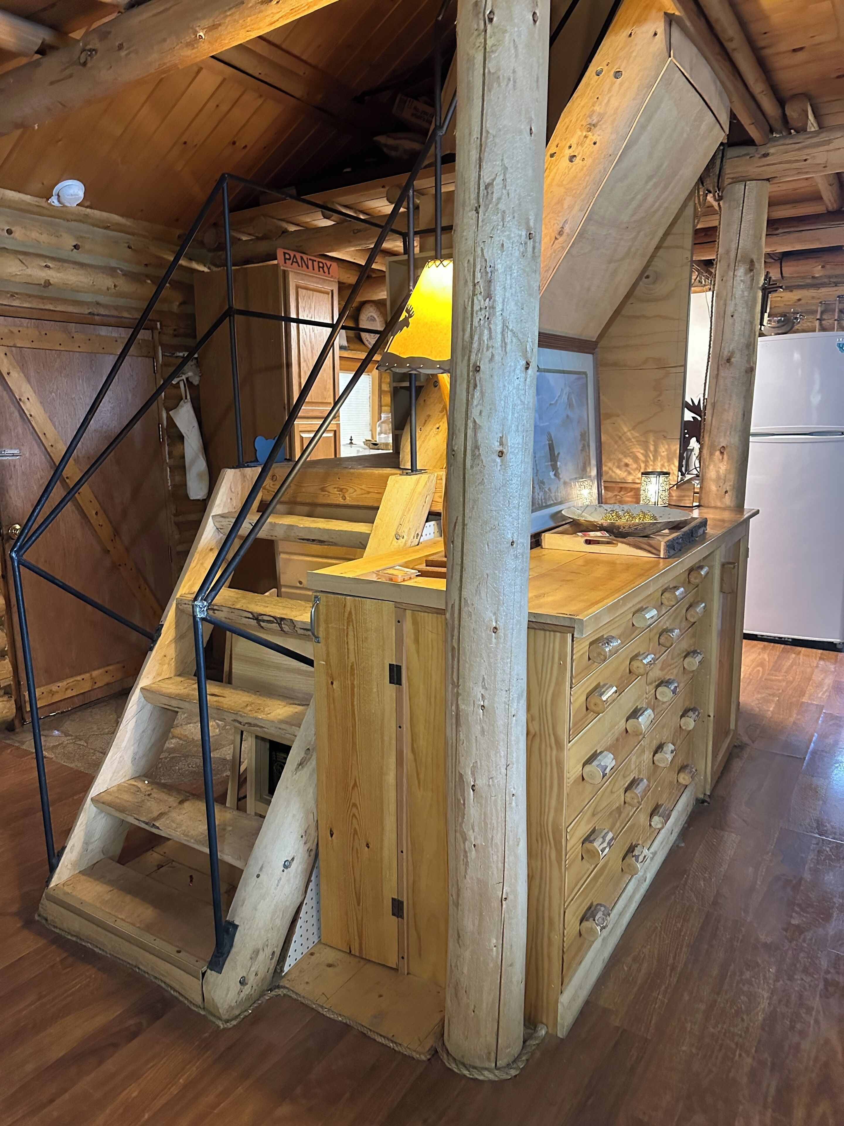 Un escalier en bois mène à un espace cuisine équipé d’un comptoir en bois et d’un réfrigérateur.