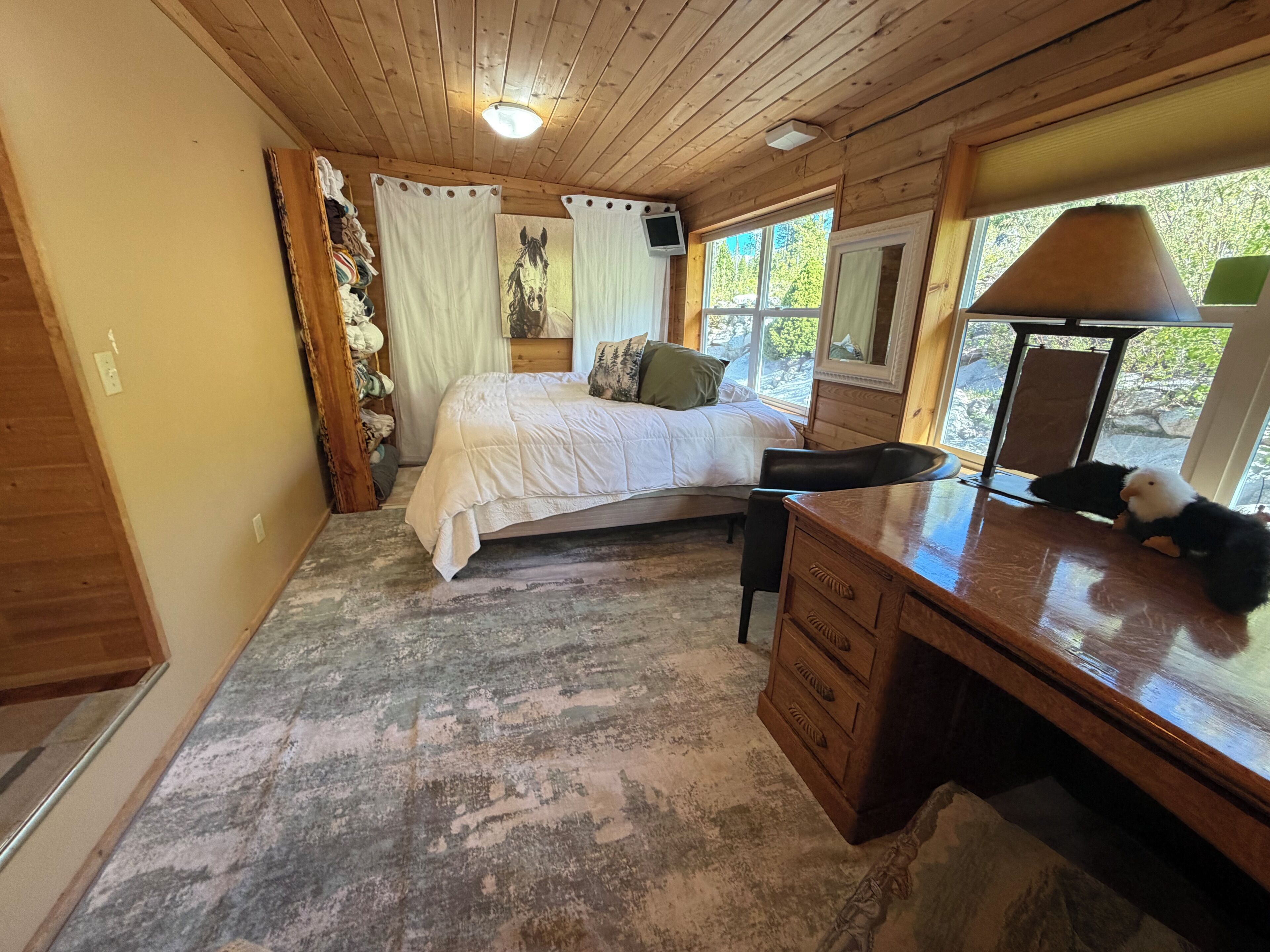 A bedroom with a bed, a desk, a chair, a lamp, and a window with a view of trees.