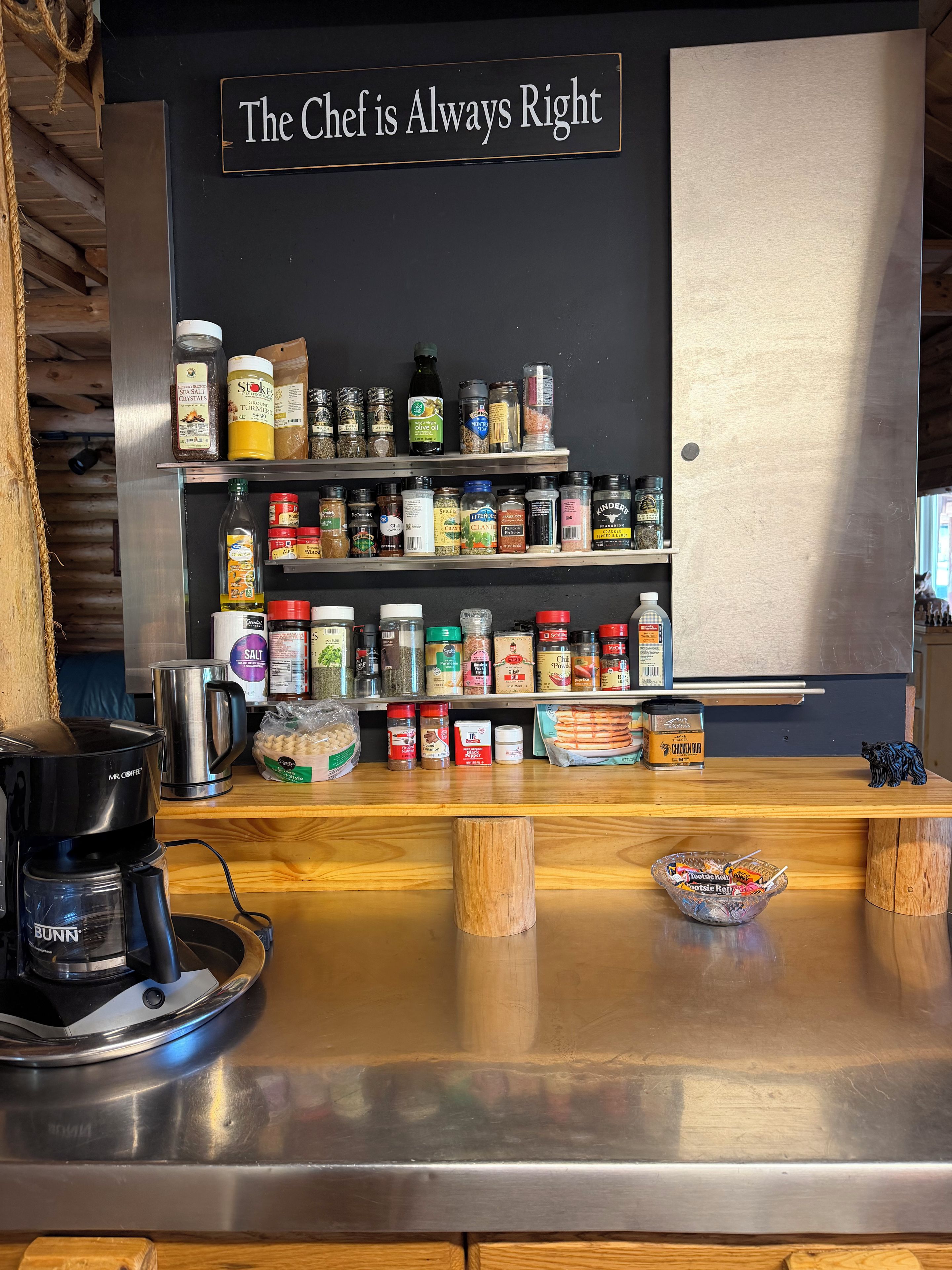 Una encimera de cocina con diversos condimentos y especias, una cafetera y un letrero que dice 'The Chef is Always Right'.