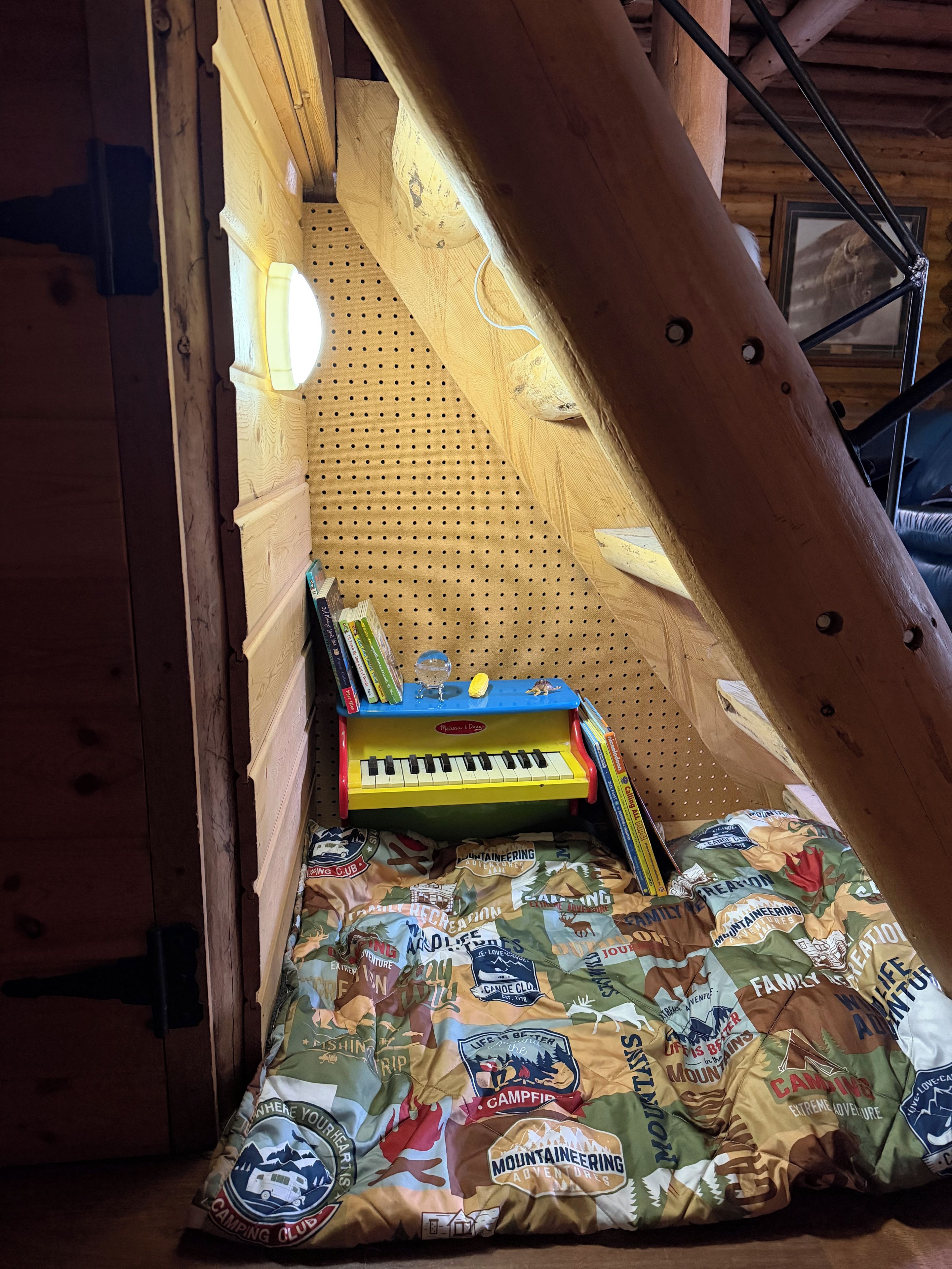 Un dormitorio tipo loft con techo inclinado de madera, un pequeño piano y un colchón con motivos de campamento.