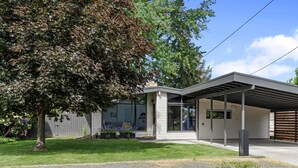 Een modern huis met een overdekte garage, een grote boom en een verzorgd gazon.