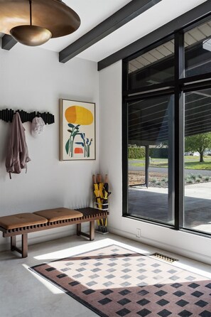 Ein modernes Interieur mit einer Bank, einem gemusterten Teppich, einer Pendelleuchte und einem großen Fenster.