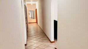 Un pasillo estrecho con suelo de baldosas, paredes blancas y una puerta de madera al final.