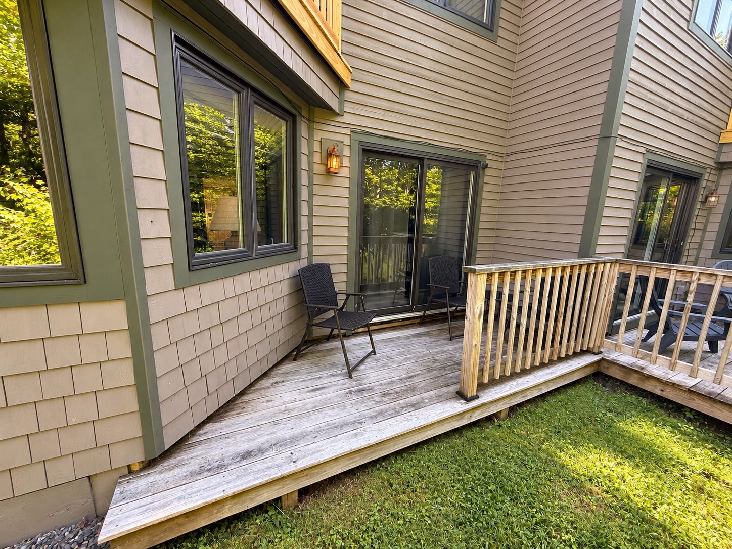A deck with a wooden railing, a chair, and a window with a view of greenery.