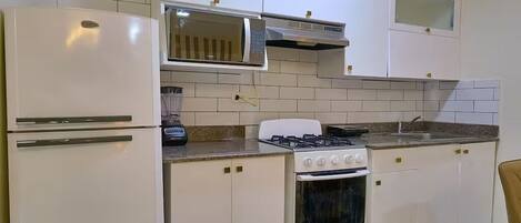 Una cocina con armarios blancos, estufa, microondas y refrigerador.