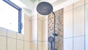 Une douche équipée d’un pommeau réglable, d’un panneau de commande fixé au mur et d’un sol carrelé.
