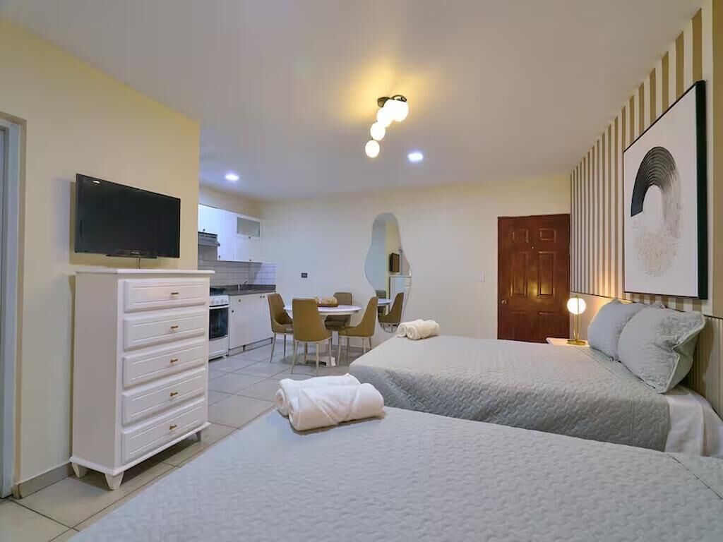 Habitación de hotel con dos camas, televisión, escritorio y zona de comedor.