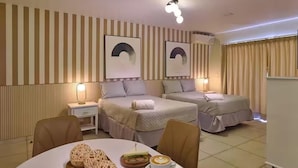 Une chambre d’hôtel avec deux lits, une table à manger mise pour le petit-déjeuner et des œuvres d’art accrochées aux murs.